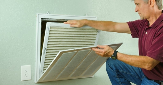 photo of a man inspecting the air filter behind a home vent