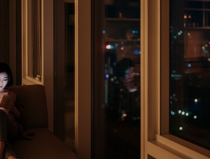 woman sitting by window at night looking at phone.